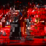 A man mixing a cocktail in a bar that has subdued red lighting.