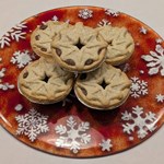 Five mince pies with star-shaped pastry tops arranged on a festive red plate decorated with white snowflakes.