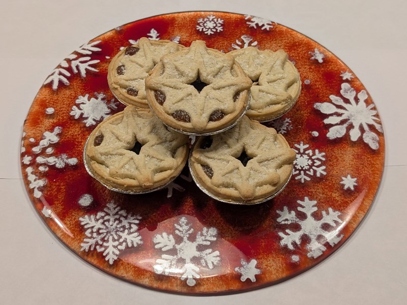 Five mince pies with star-shaped pastry tops arranged on a festive red plate decorated with white snowflakes.