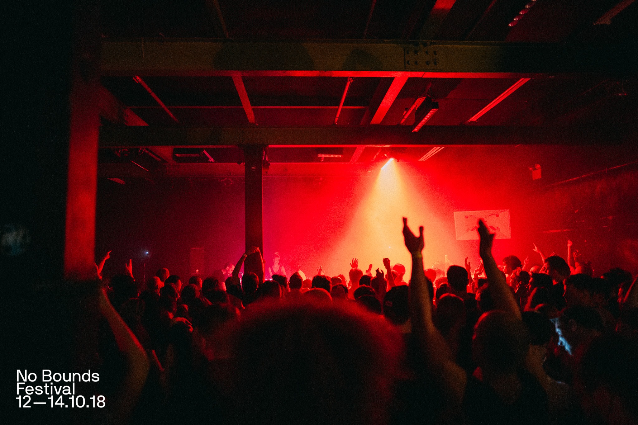 A night club lit by red light is packed with people dancing to music.