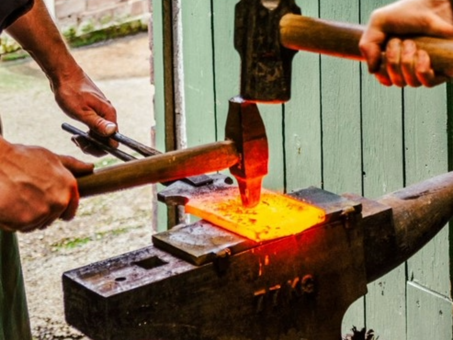 A close-up of two people forging a piece of metal on an anvil.