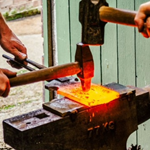 A close-up of two people forging a piece of metal on an anvil.