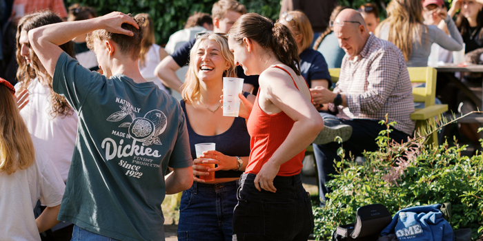 A group of people in a pub garden, enjoying a drink in the sunshine.