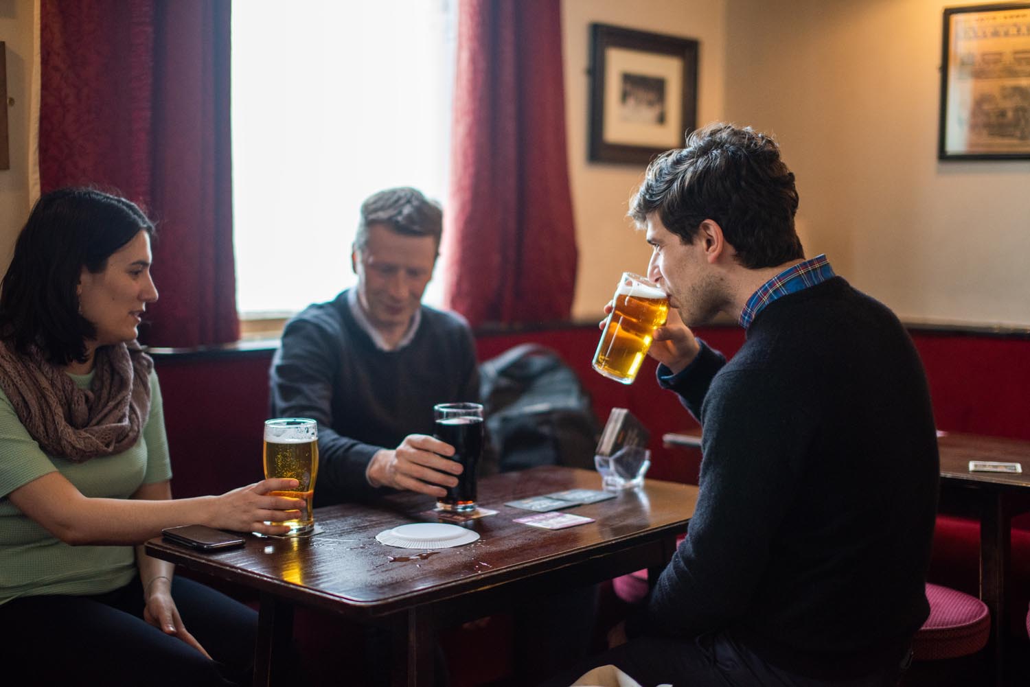 Three people sat round a pub table enjoying a beer.