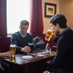Three people sat round a pub table enjoying a beer.