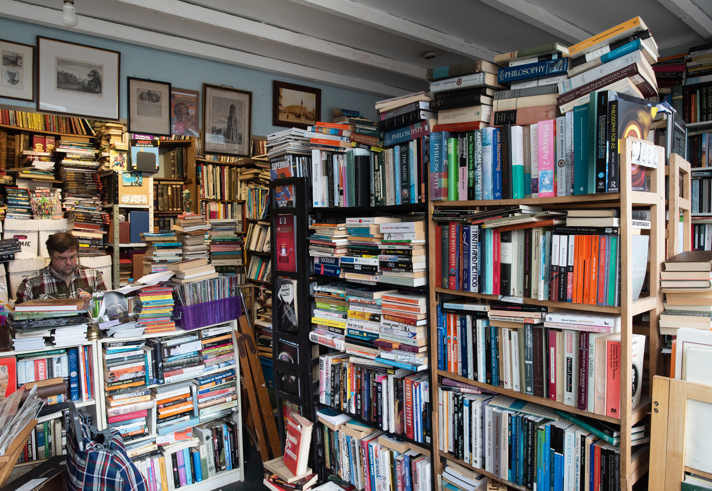 Interior of Porter Book Shop showing tall, densely packed bookshelves filled with a wide variety of second‑hand books. The room is full of stacked books, framed artwork on the walls, and an eclectic, cosy atmosphere typical of a classic used bookshop.