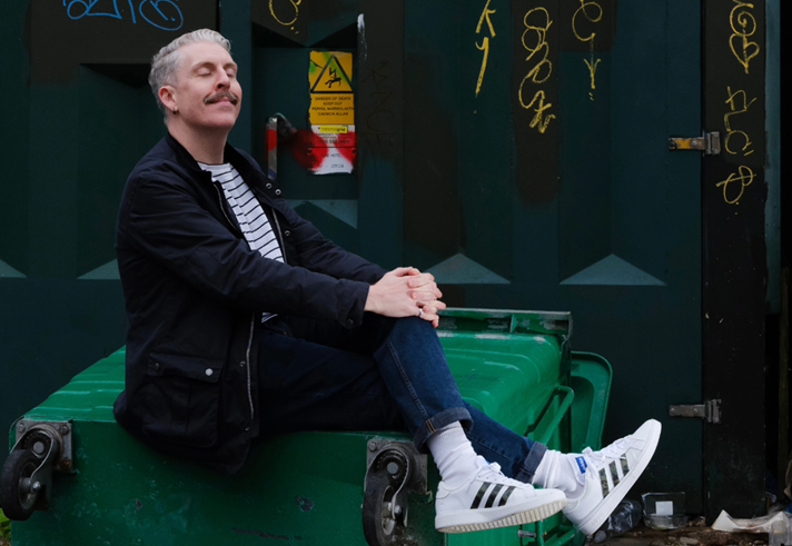A photo of Carl Donnelly, sitting on a huge industrial rubbish bin.