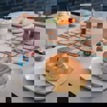 A bagel on a plate and a milkshake, sat on a table that also has a board game set up on it.