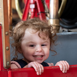A small child is having fun and playing on an old fashioned fire engine in a museum.
