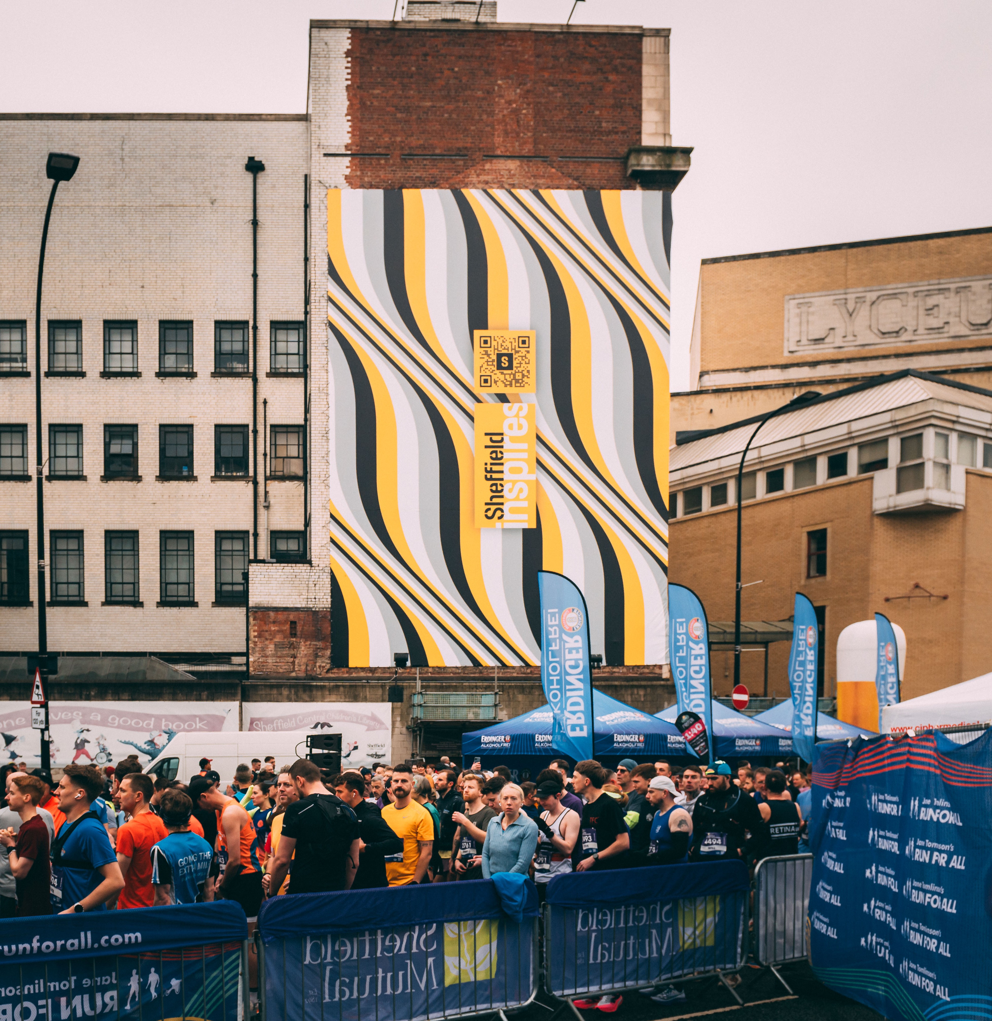 A massive banner on the side of the building shows the distinctive Sheffield Inspires branding as runners gather for Sheffield Half Marathon below it 