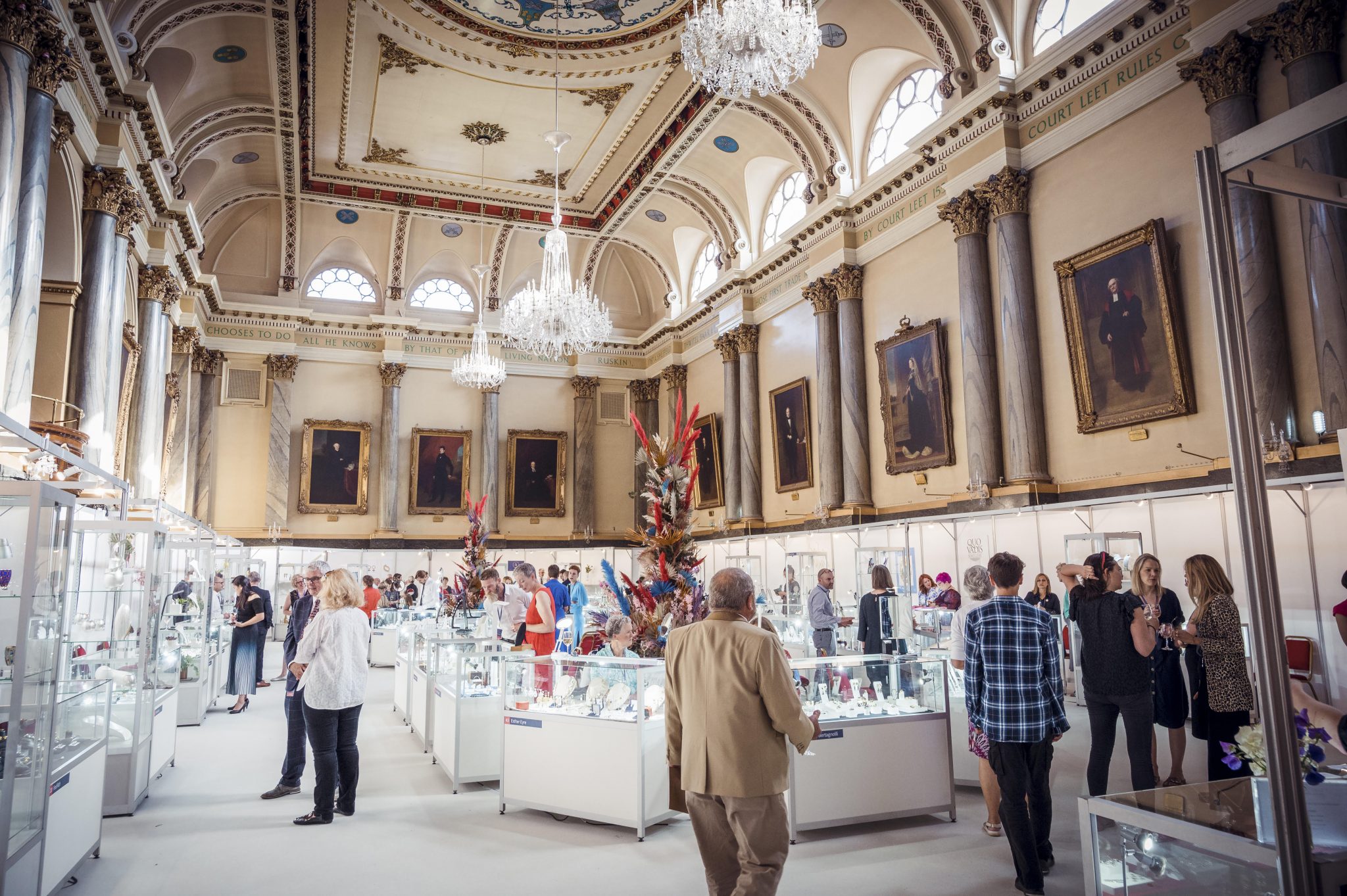 The interior of Cutlers' Hall set up for the Goldsmiths North event. The room is filled with glass display cases and lavish floral displays.