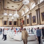 The interior of Cutlers' Hall set up for the Goldsmiths North event. The room is filled with glass display cases and lavish floral displays.