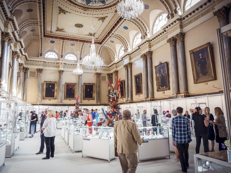 The interior of Cutlers' Hall set up for the Goldsmiths North event. The room is filled with glass display cases and lavish floral displays.