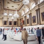 The interior of Cutlers' Hall set up for the Goldsmiths North event. The room is filled with glass display cases and lavish floral displays.