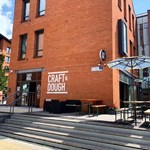 The exterior of Craft And Dough, a red brick building, with their logo painted on the wall.