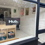 The window of a record store with a sign in the window that reads 'HUB.' . In the shop you can see wooden racks filled with vinyl records.
