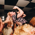 A singer is being lifted up by the crowd at a gig.