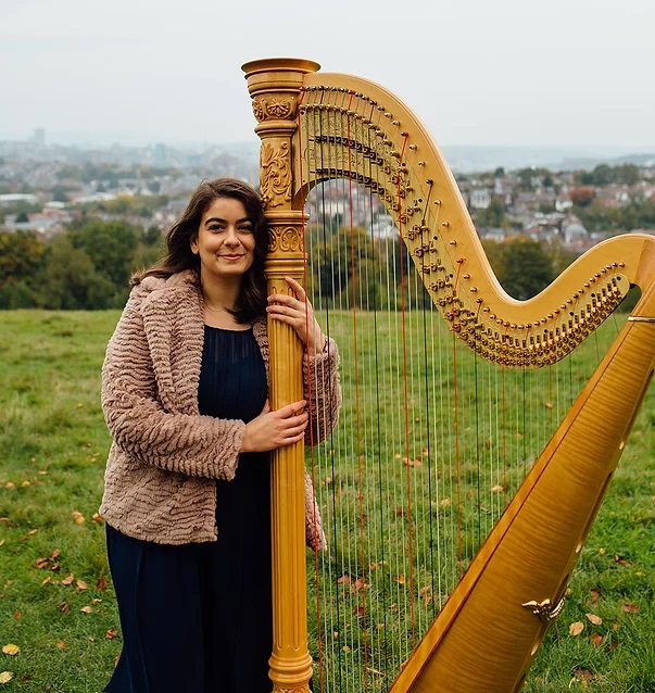 Imogen Garnettand her harp, in a field.