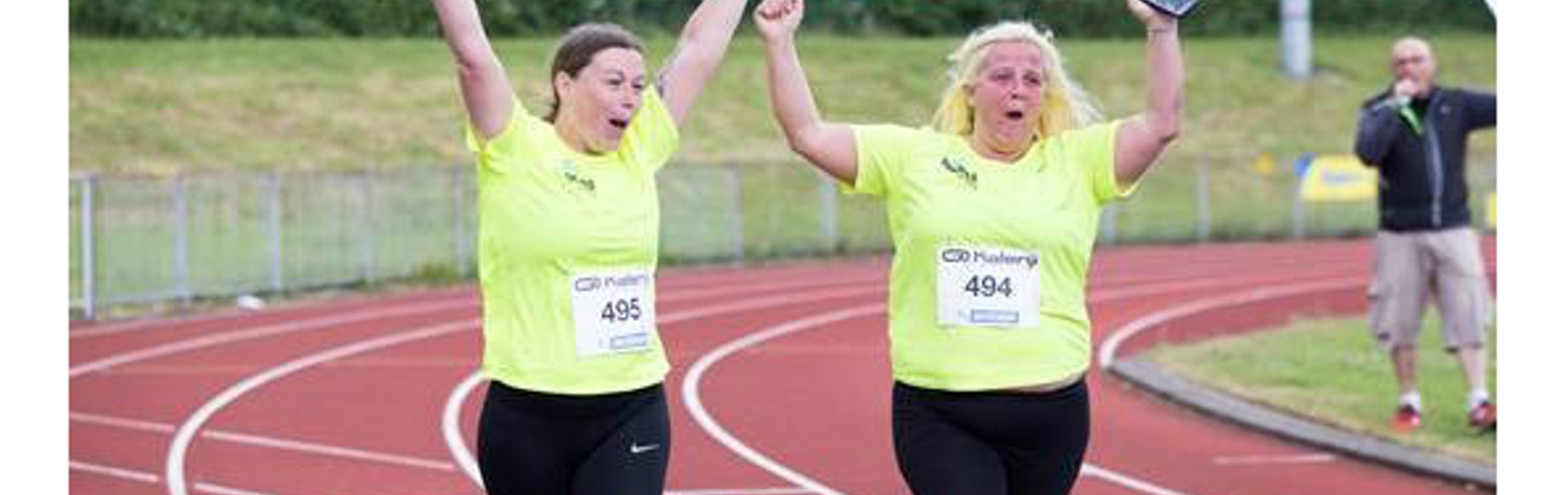 People on a race track, wearing running clothing, with their arms in the air.