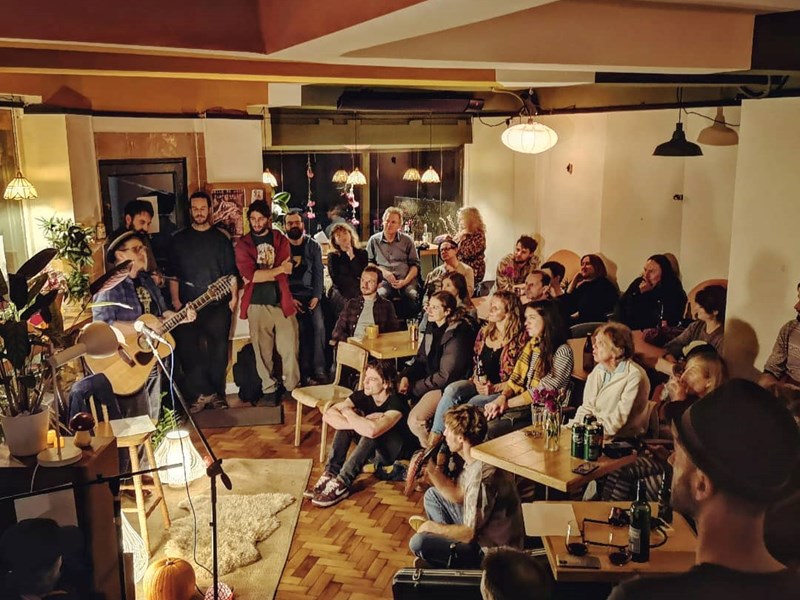 A man plays an acoustic guitar and sings in front of a small crowd at Kopi & Chai.