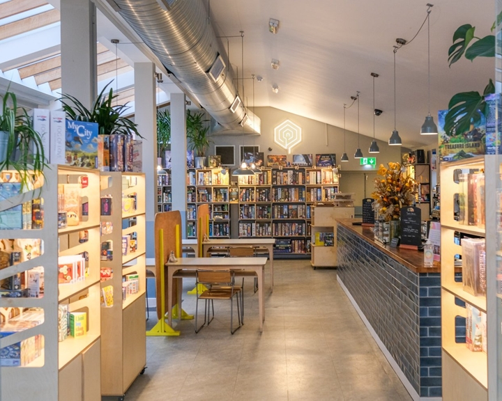 Inside the Boardgames café with rows of shelves stacked up with games, lots of tables and chairs and a service counter along one wall.