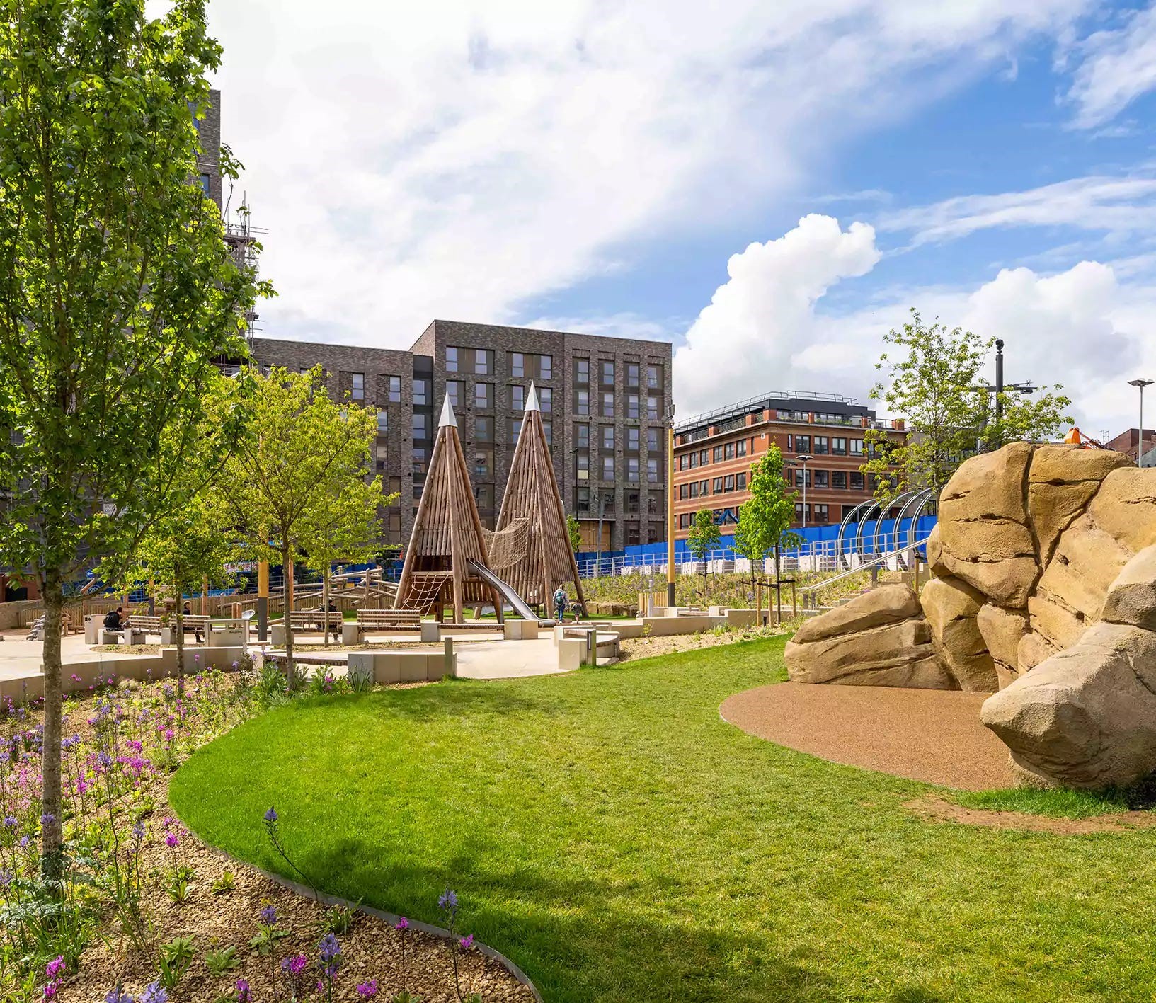 A grassy area in Pound's Park flanked by big boulders and play equipment.