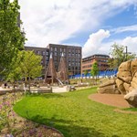 A grassy area in Pound's Park flanked by big boulders and play equipment.