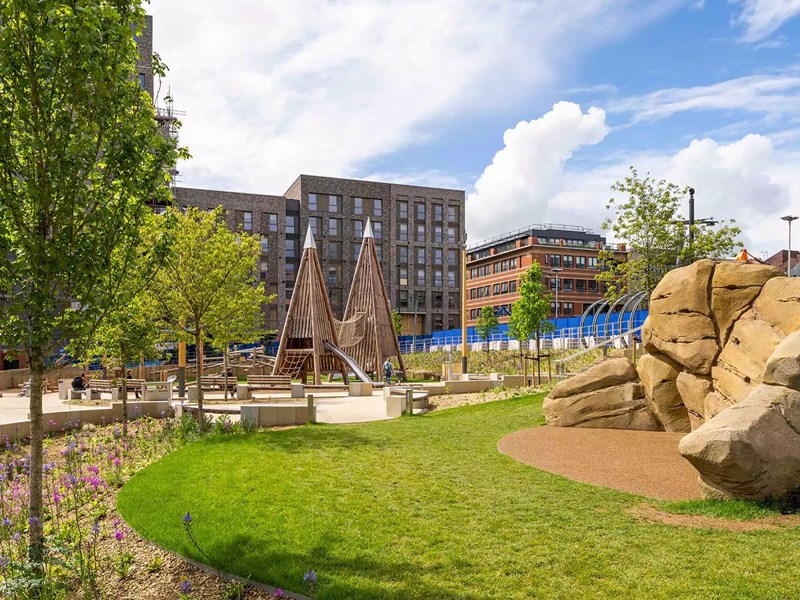 A grassy area in Pound's Park flanked by big boulders and play equipment.
