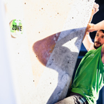 A man is climbing on the corner of a wall. He has one hand holding onto the wall vertically and another held onto the wall horizontally.