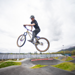 A person, on a BMX style bike, in midair while cycling round a pump track.