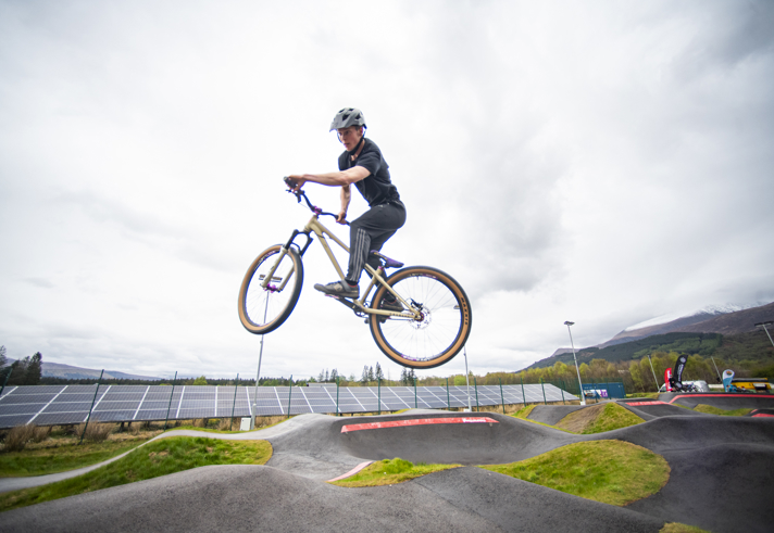 A person, on a BMX style bike, in midair while cycling round a pump track.