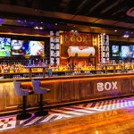 Long bar with illuminated signage and multiple large screens showing sport