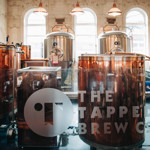 Close-up of stainless steel and copper brewing tanks inside the Sheffield Tap, with the Tapped Brew Co logo visible on the glass barrier in front.