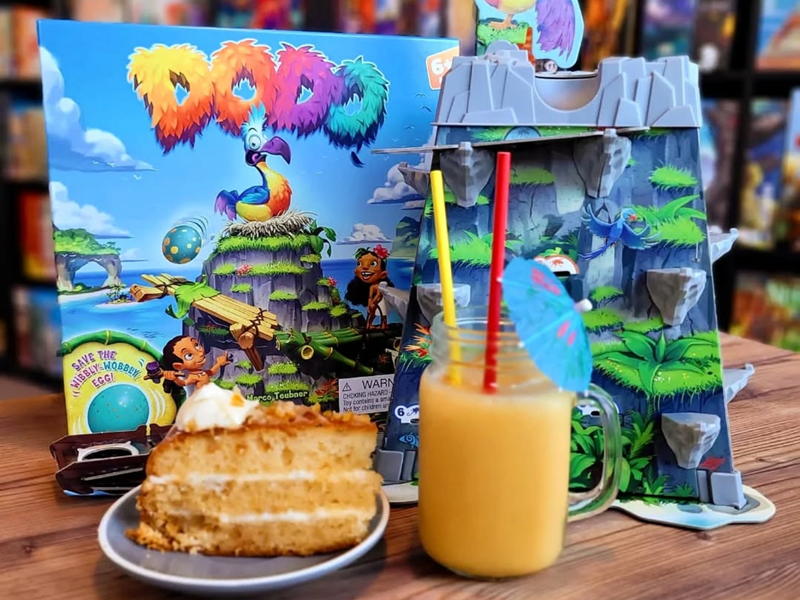 A table at The Dice Box Sheffield with a cocktail, a slice of cake and a game called Dodo.