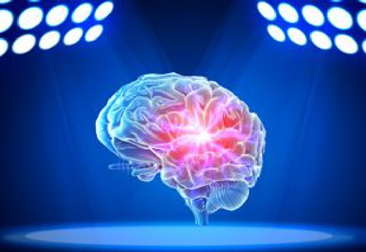 A glowing, semi‑transparent digital illustration of a human brain is shown floating at the center of a dark blue spotlighted stage. Bright white and blue lights arranged in circular clusters shine down from the upper left and upper right corners, illuminating the brain. The center of the brain glows with an intense red and pink light, highlighting internal structures against the deep blue background.