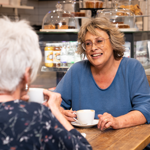 Two women sit at a table, drinking coffee and chatting.