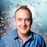 A portrait of Jimeoin. Behind him there is loads of confetti flying about.