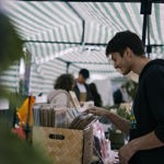 A man wearing a hoodie browsing through a box of vinyls