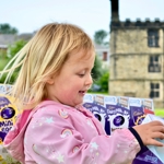 A child, standing in an outdoor setting, is holding a chocolate Easter egg in a box.