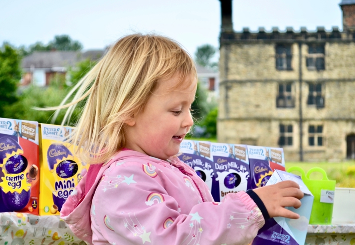 A child, standing in an outdoor setting, is holding a chocolate Easter egg in a box.