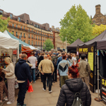 Crowds walking through an outdoor market lined with food stalls and tents in a city square