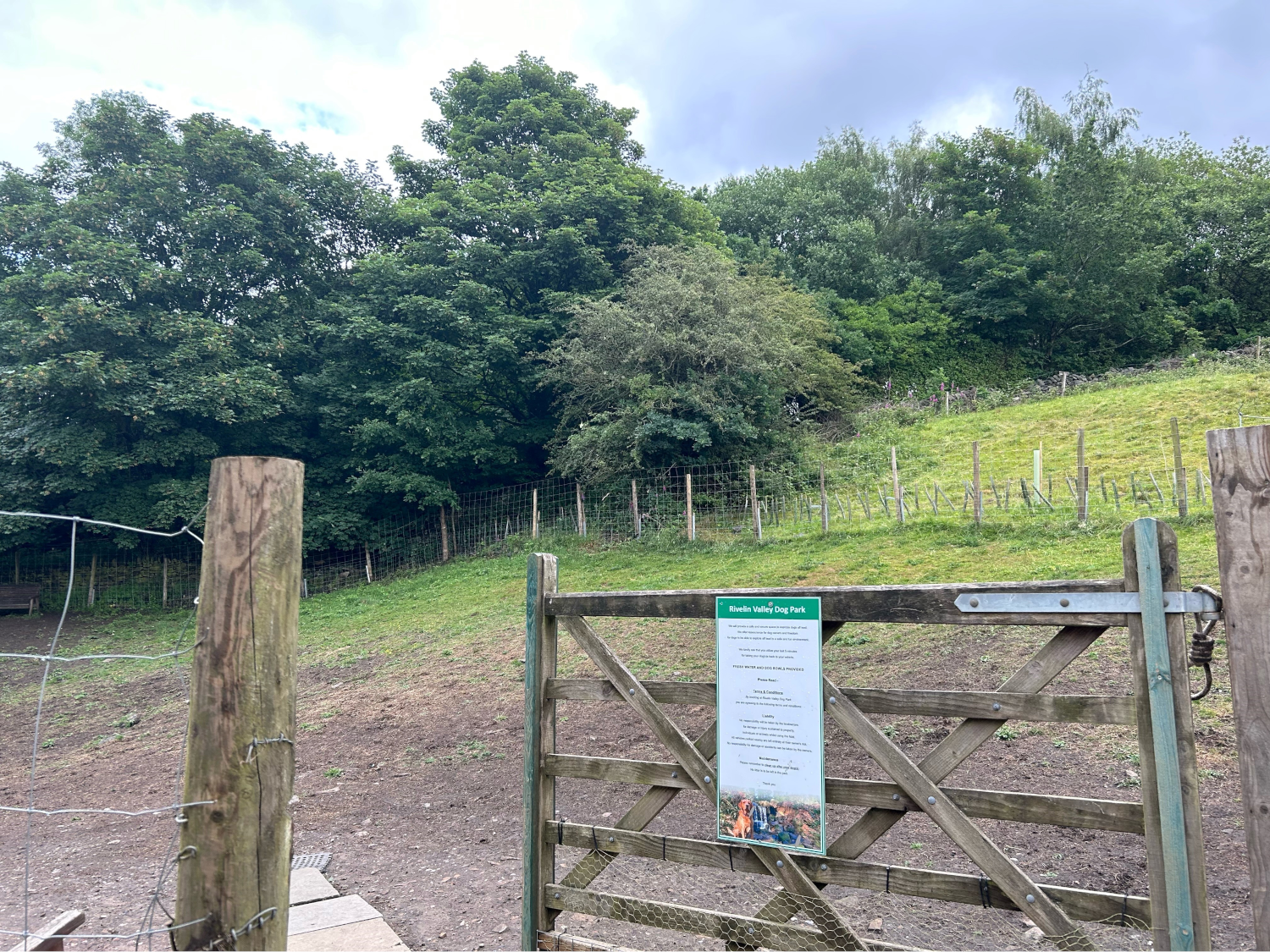 An open gate leads into a fenced off grassy field at Rivelin Valley Dog Park.