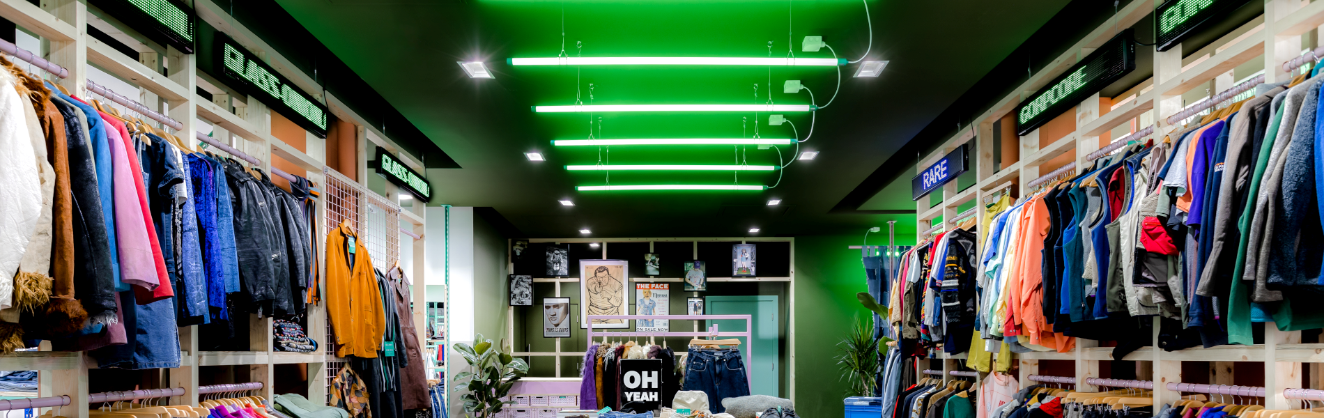Inside the Glass Onion shop. All the walls are full of clothes on rails. In the centre of the shop are tables with accessories on display.