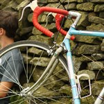 A cyclist sat leaning against a wall having a rest, out in the countryside, with his bike propped up next to him.