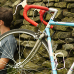 A cyclist sat leaning against a wall having a rest, out in the countryside, with his bike propped up next to him.