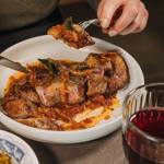 A knife and fork are shown cutting up a joint of slow cooked tender meat in a white dish