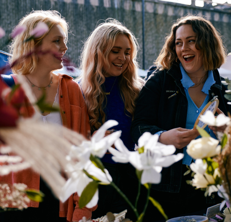 Three women looking through the goods on display on a stall at an outdoor market.