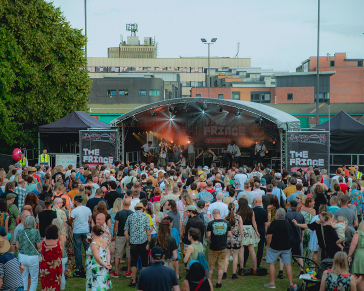 Shot from the back of a large crowd of people as they stand in front of the Devonshire Green Stage watching a band perform