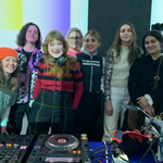 A group of people standing behind DJ decks.