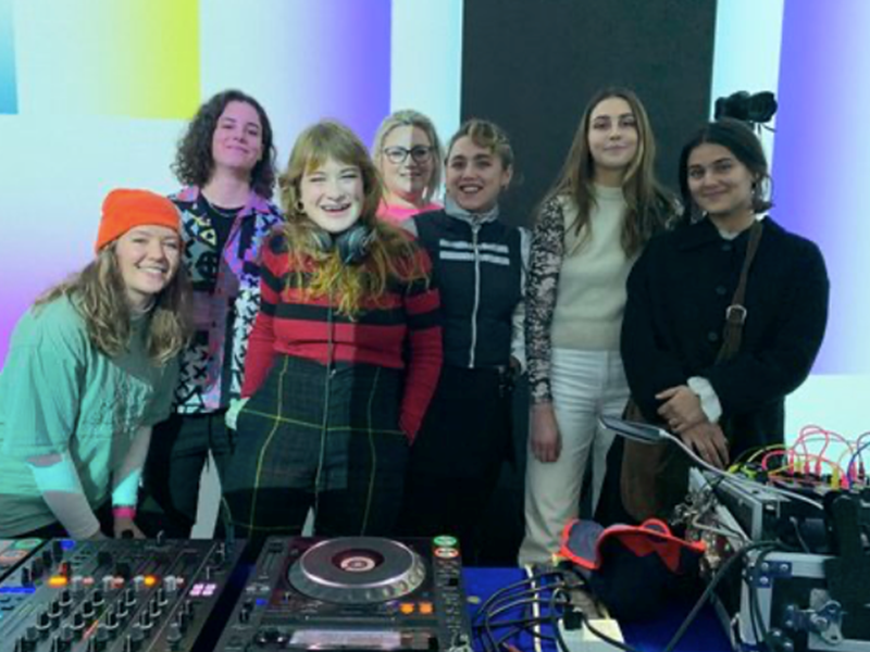 A group of people standing behind DJ decks.